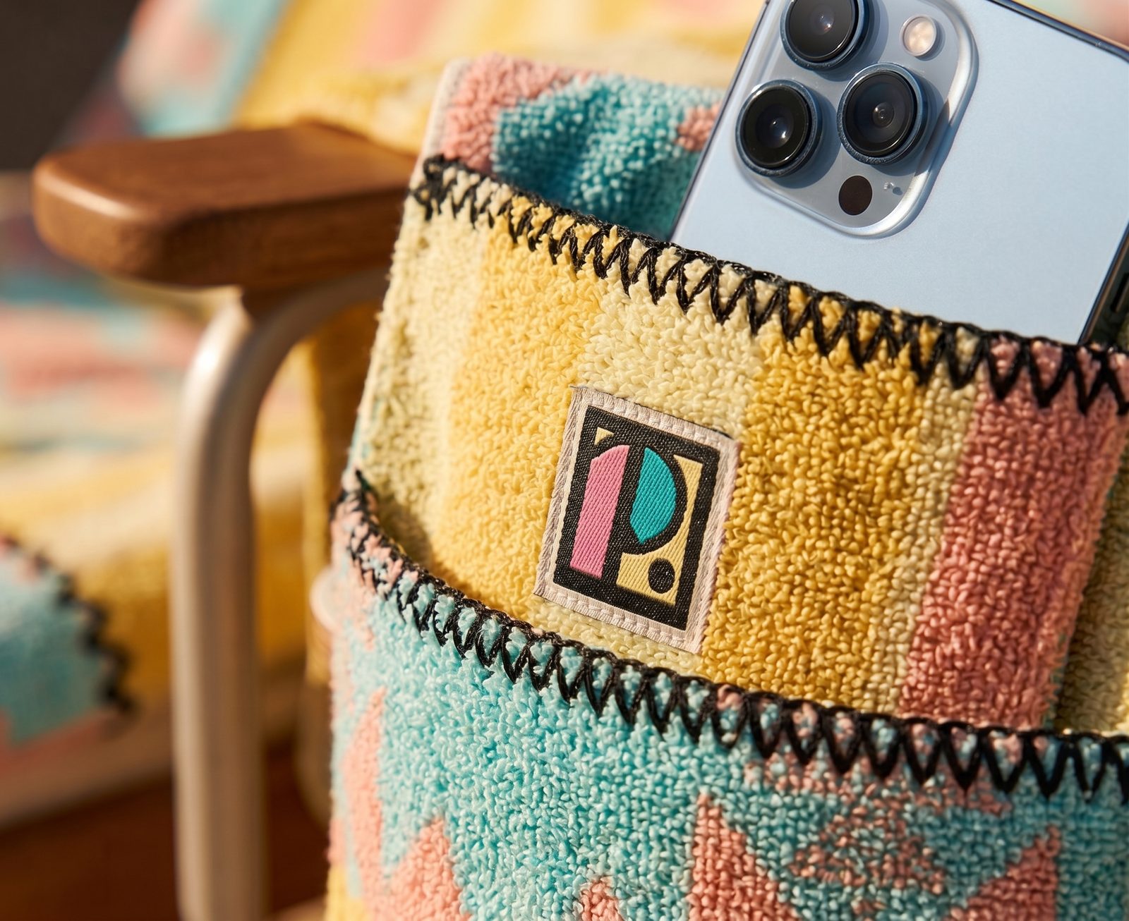 Close-up of a Lounger corner: pieced-together terry panels, zigzag edge-stitching, the woven P. label, and a phone tucked into the built-in pocket.